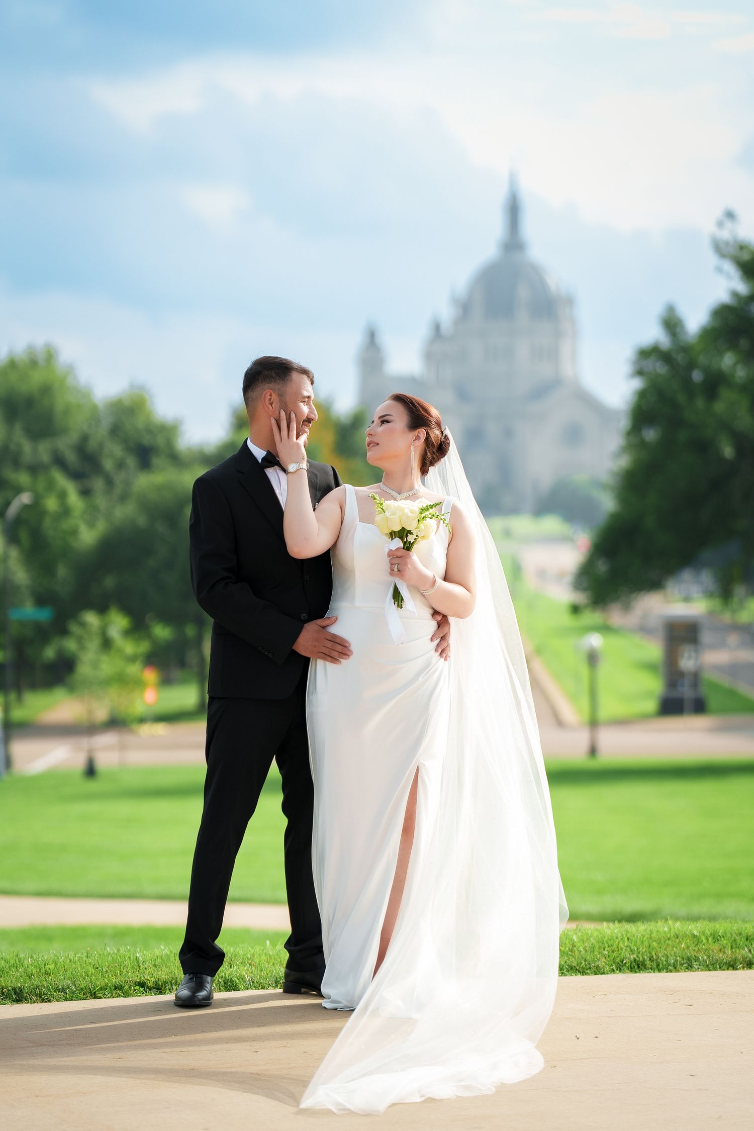 Newlyweds share romantic moments on a lawn with a grand domed building visible in the background.