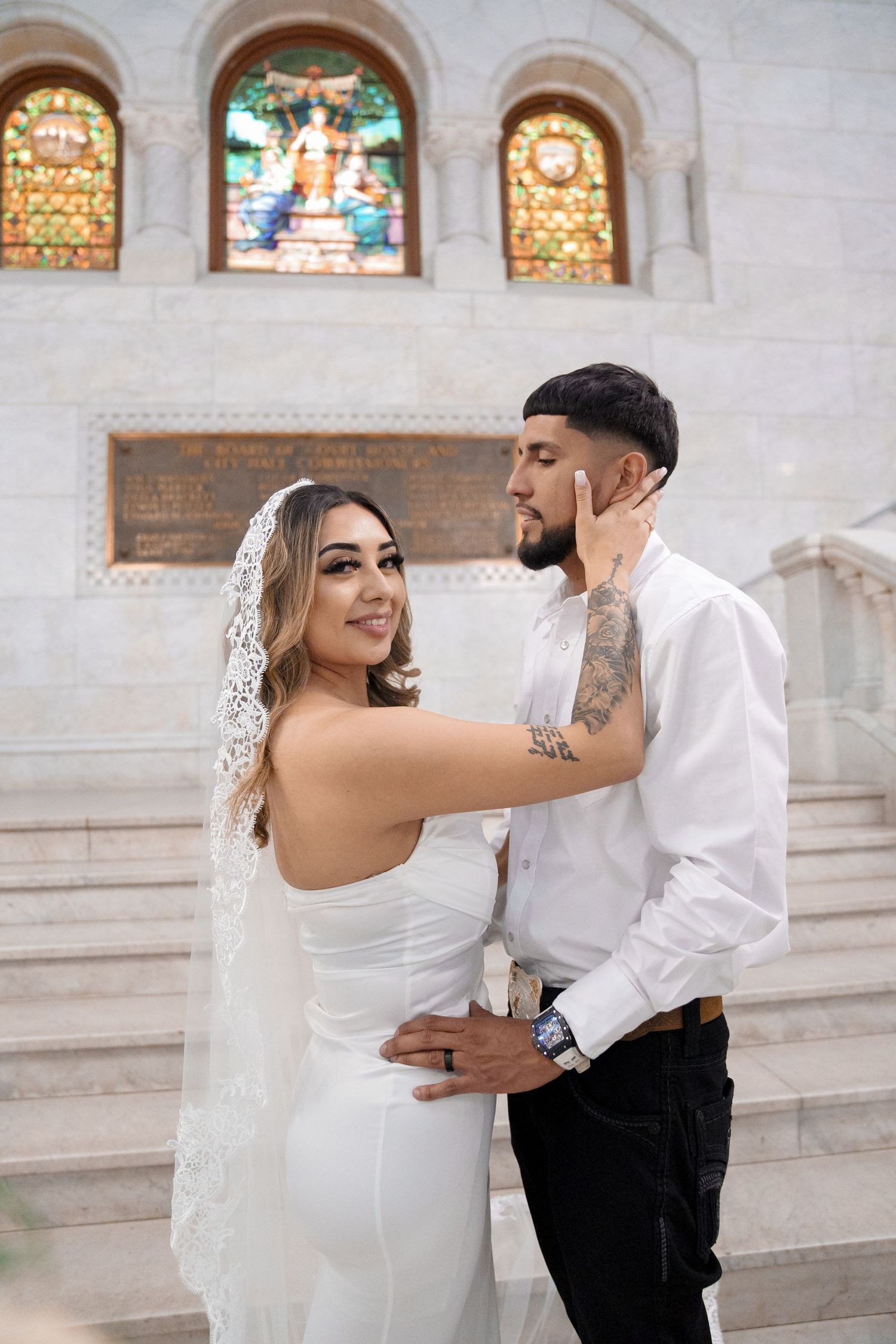 A romantic wedding couple embraces in front of stained glass windows in a church setting.