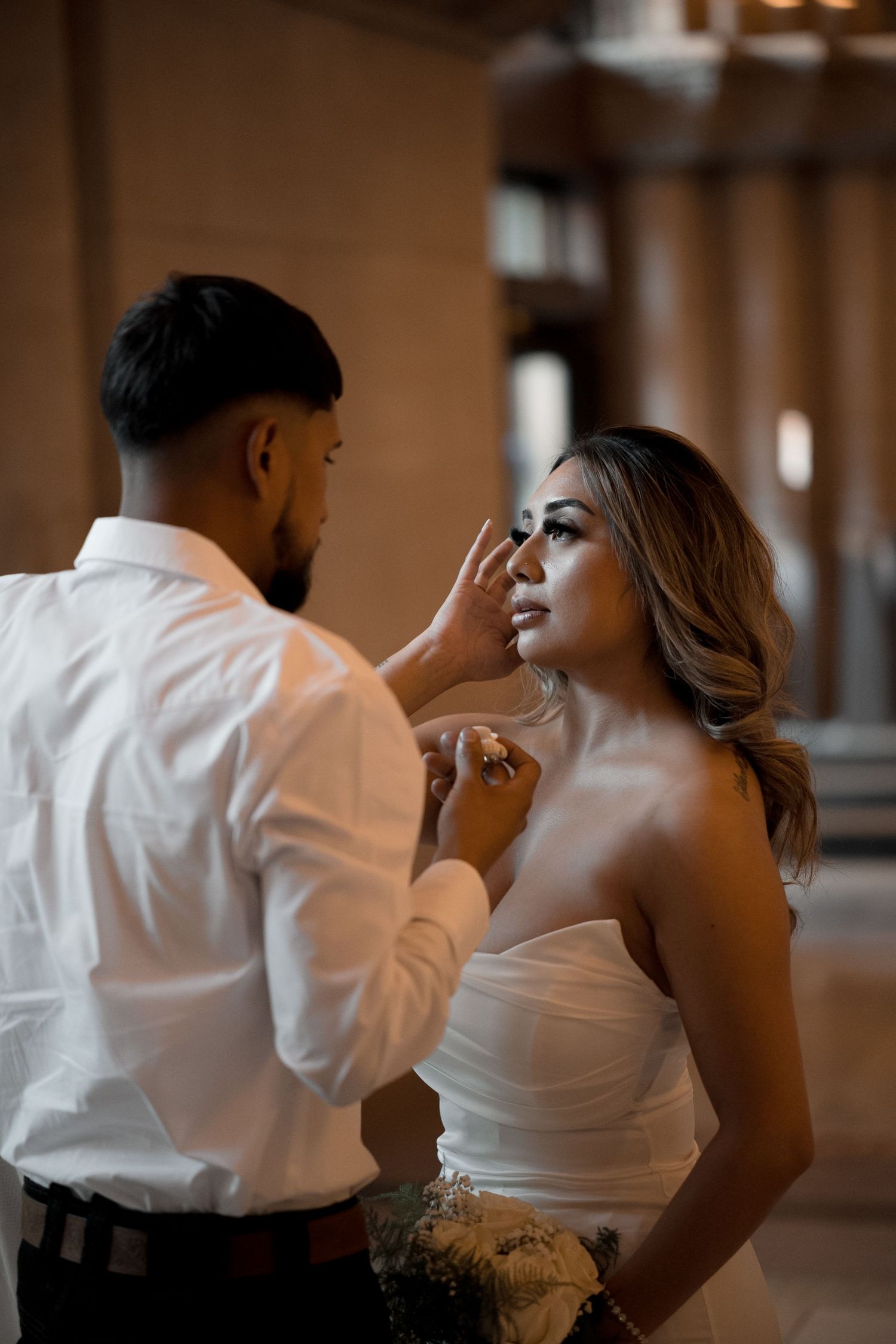 A tender moment captured as makeup is applied during wedding preparations in a dimly lit venue.