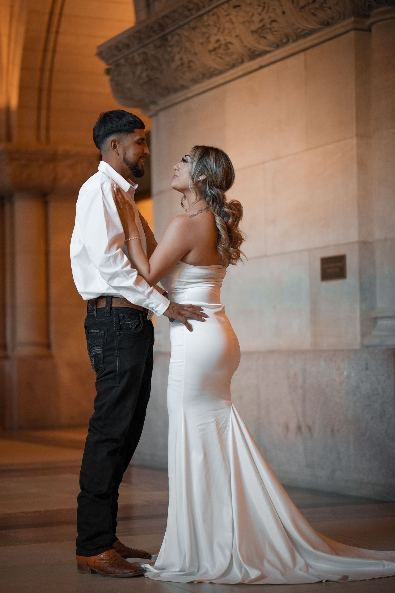 A romantic wedding couple shares an intimate moment in an elegant hallway with ornate architectural details.