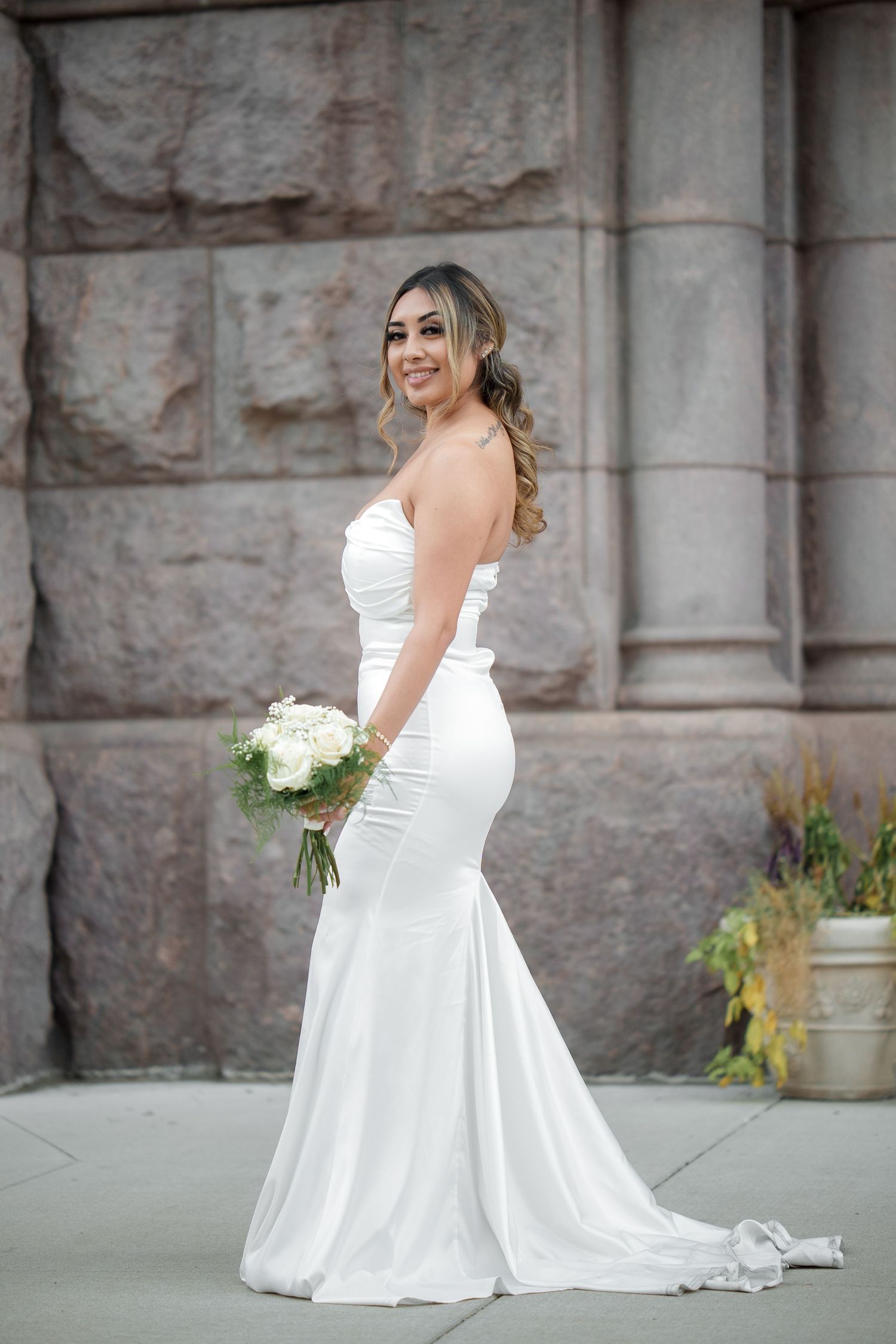 A bride in a white gown poses gracefully against a stone wall backdrop.