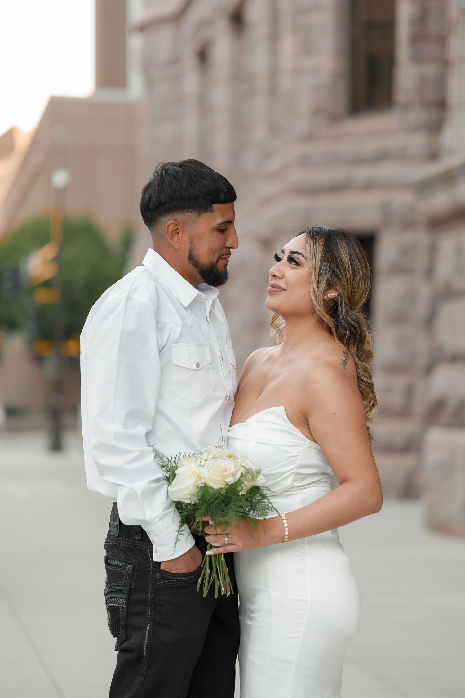 A romantic wedding couple embraces outside a stone building in an elegant photoshoot.