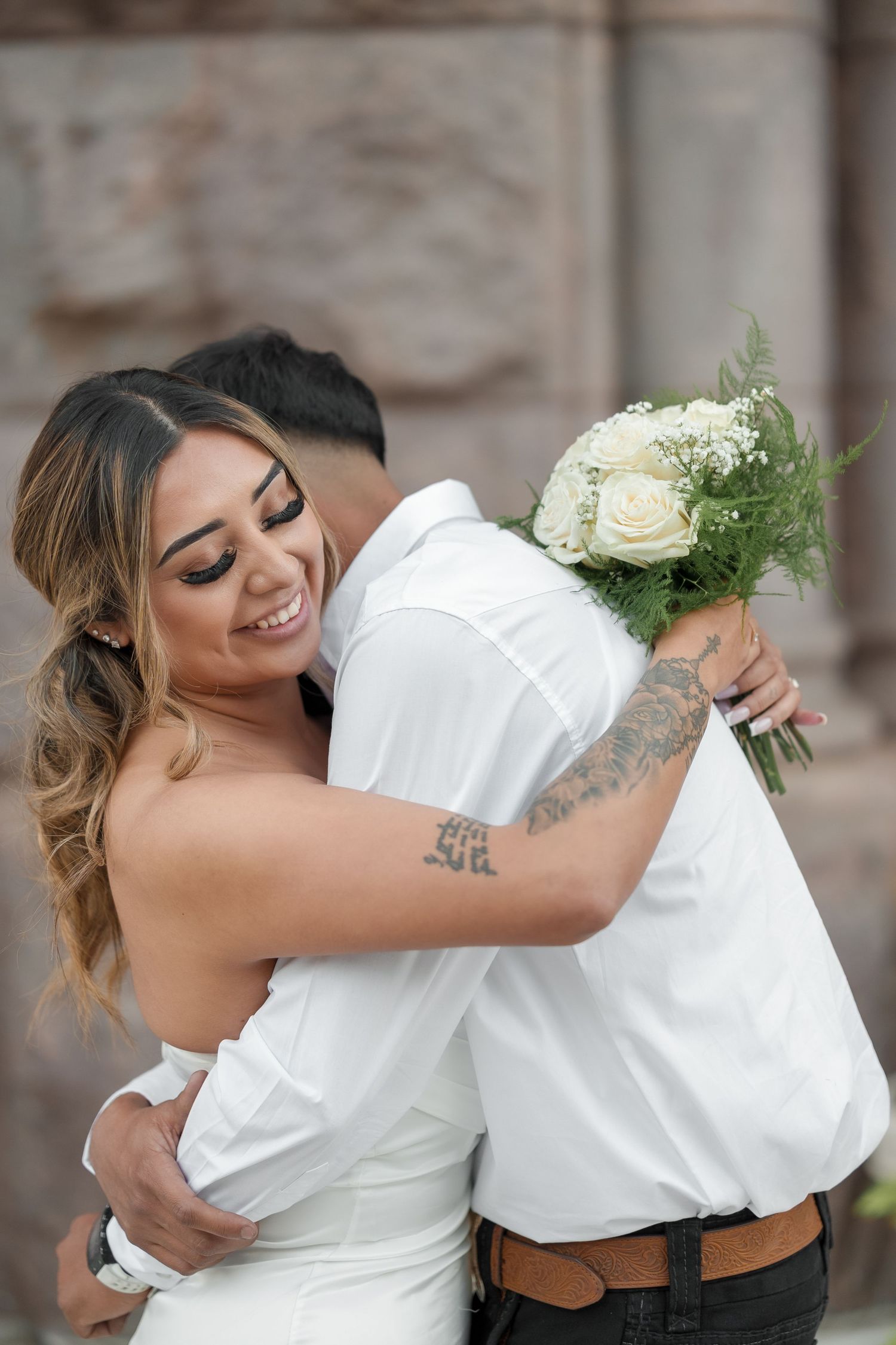 A joyful wedding couple embraces and dances together while holding a white rose bouquet.