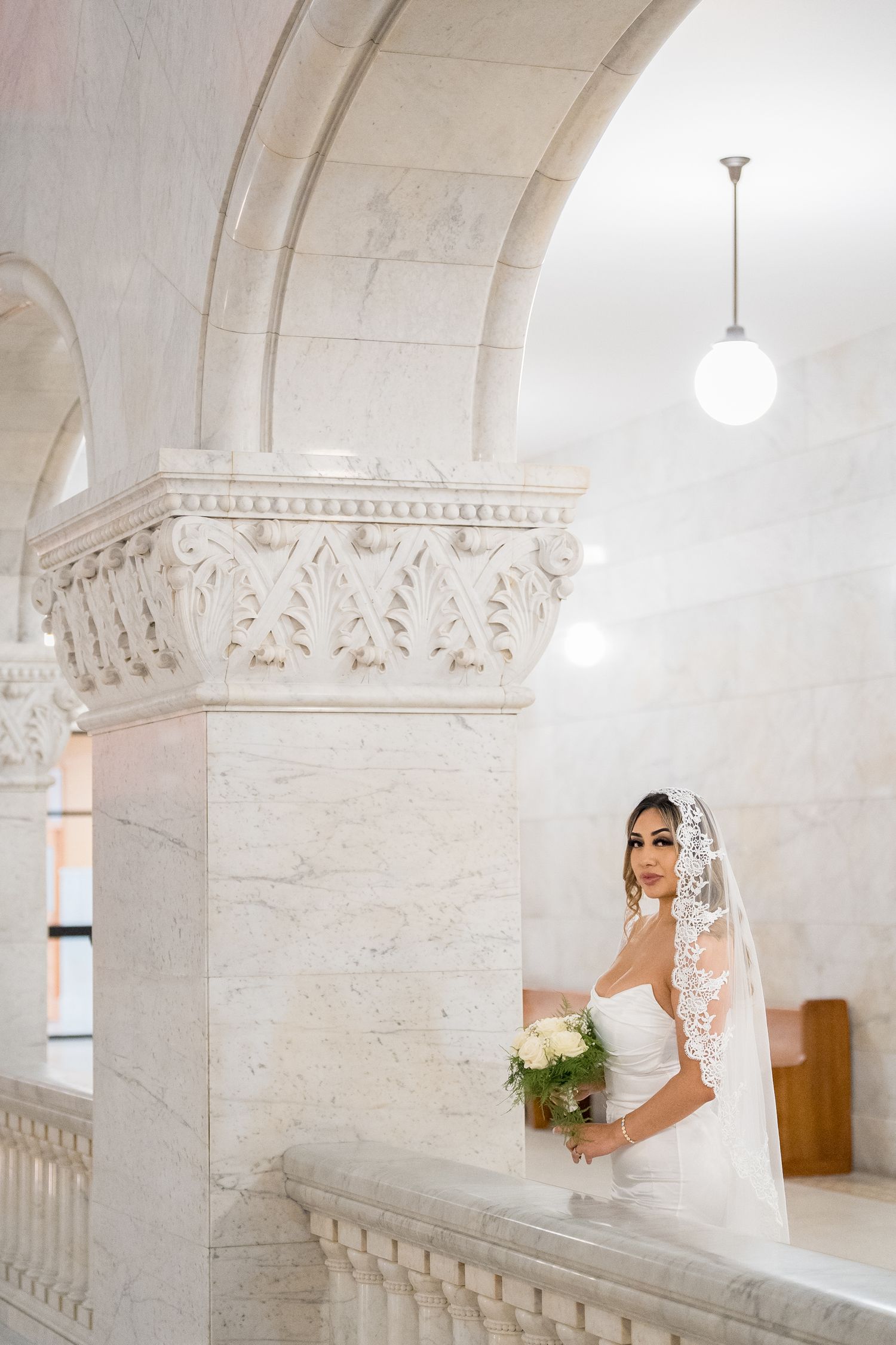 A bridal photoshoot in an elegant white stone interior with ornate architectural columns and arches.