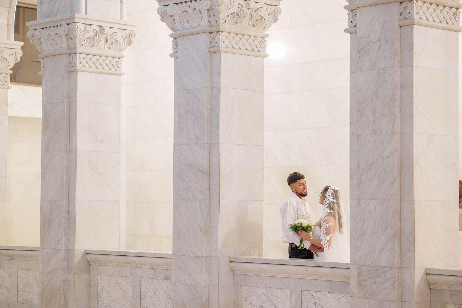 A person stands between ornate white marble columns at Arlington National Cemetery on a sunny day.