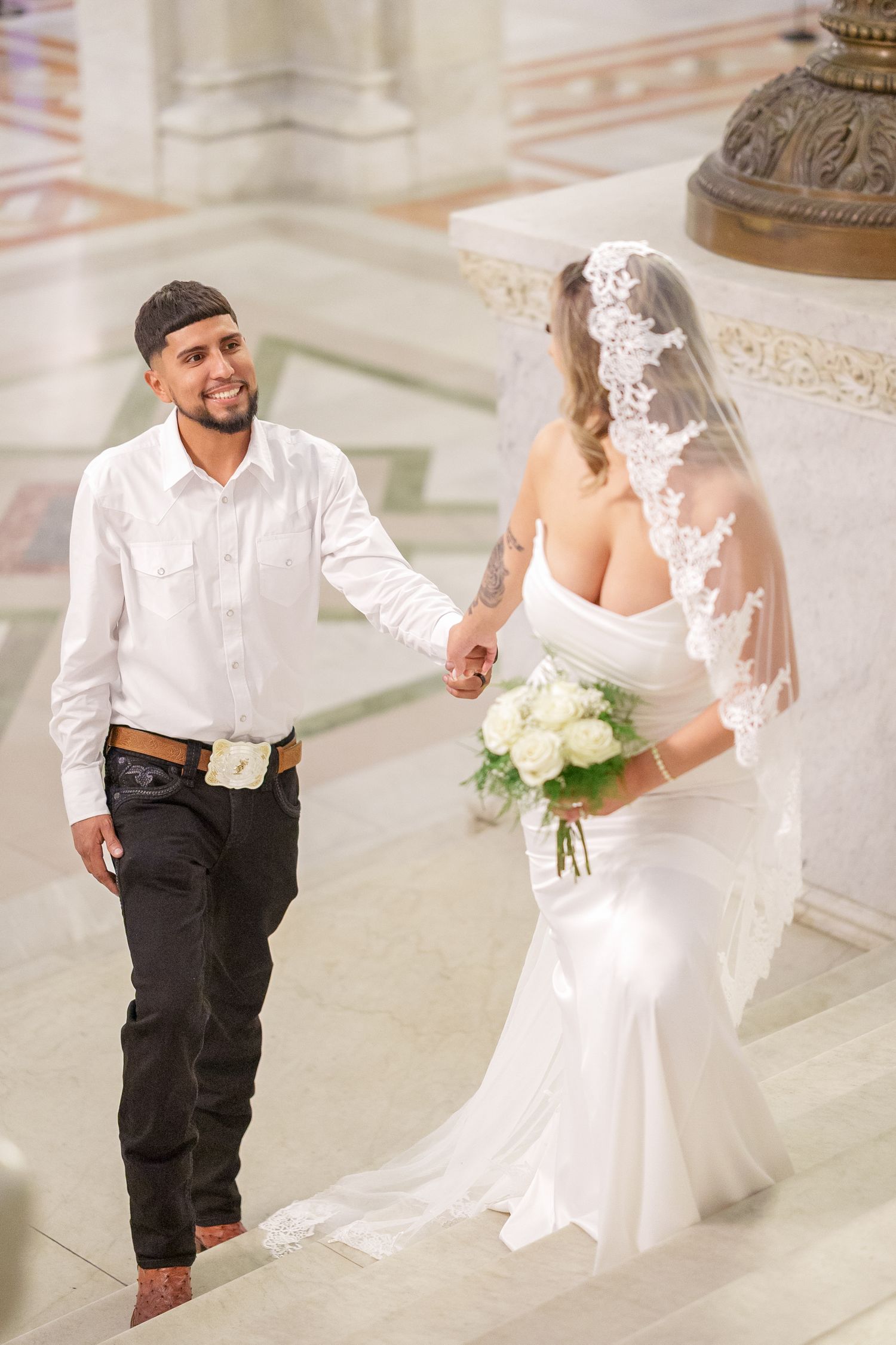 A couple walking down marble steps during their wedding, with the bride holding a white bouquet.
