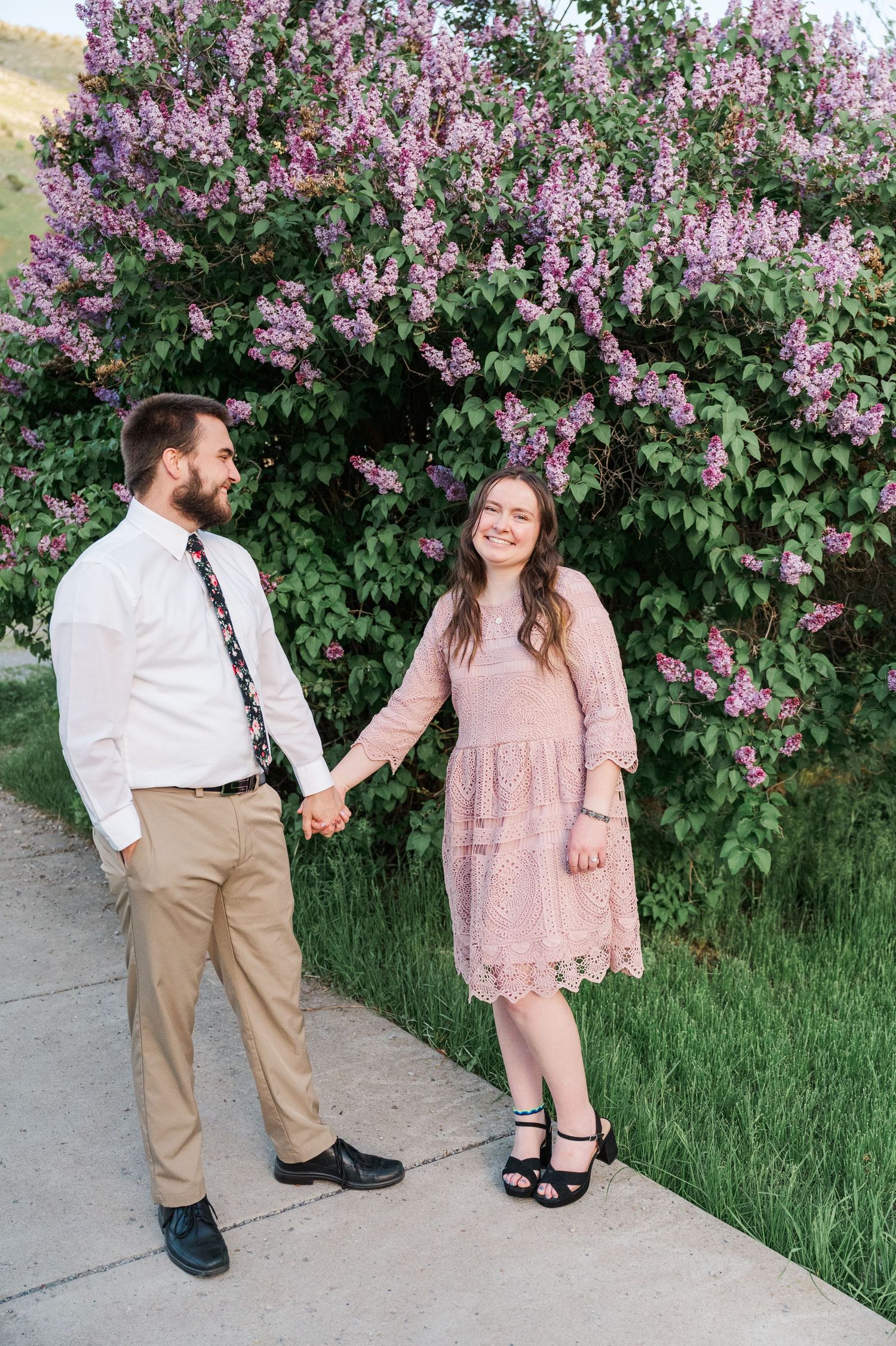 Couple holding hands by lilac bush during spring photoshoot.