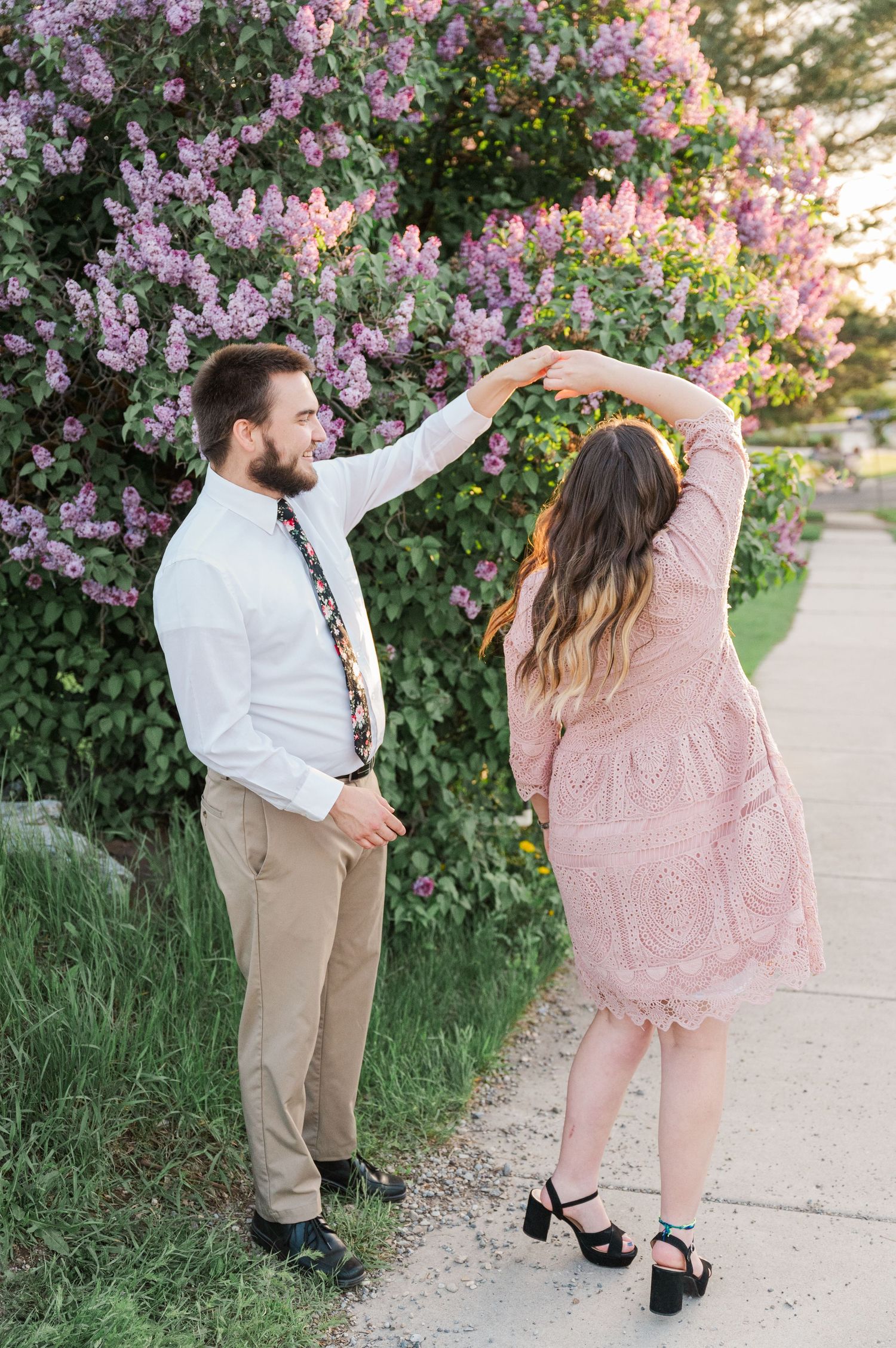 Dancing couple poses in front of blooming lilac bush during spring photoshoot.