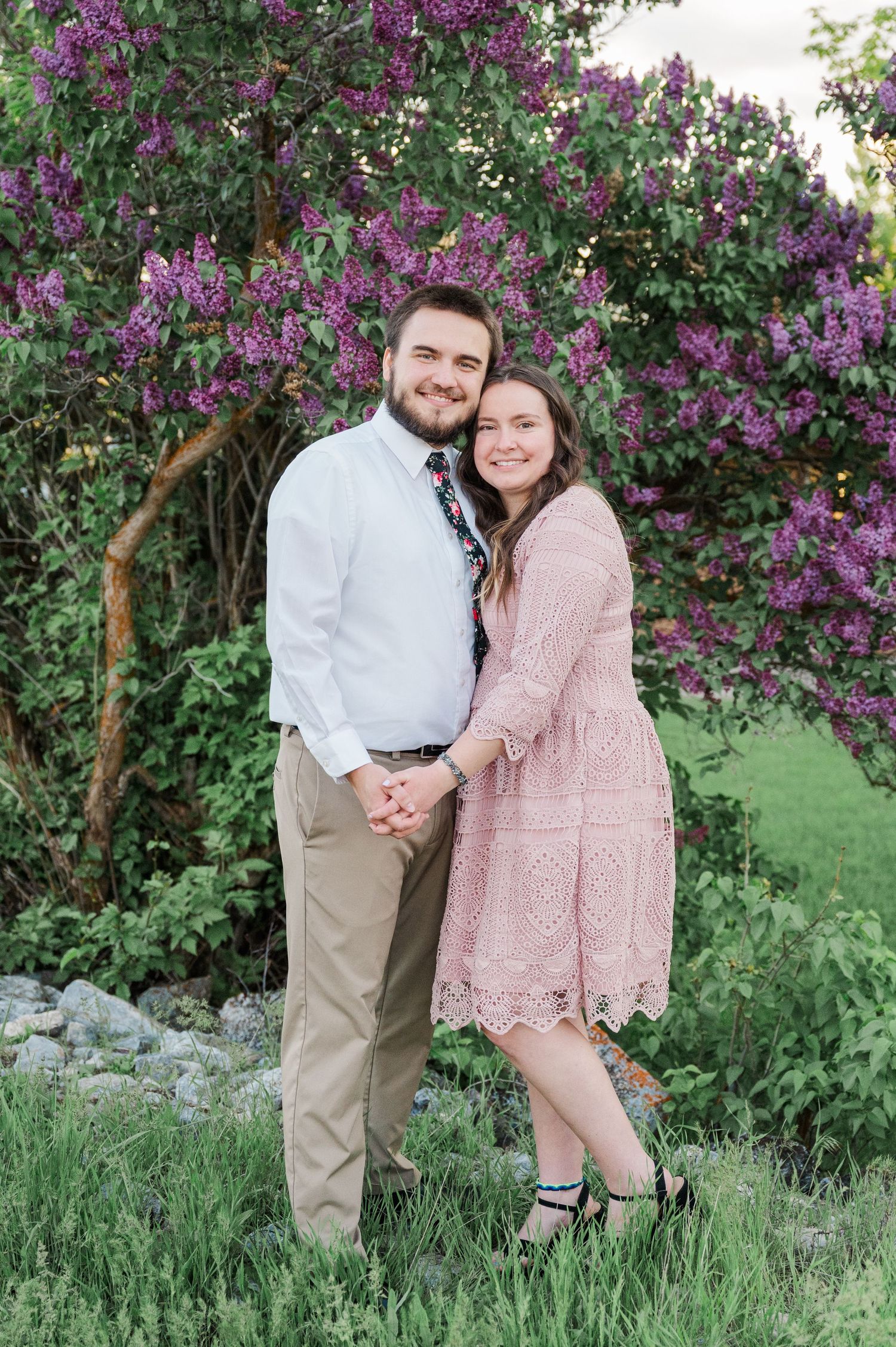 Spring engagement photo with couple posing by blooming lilac bush.