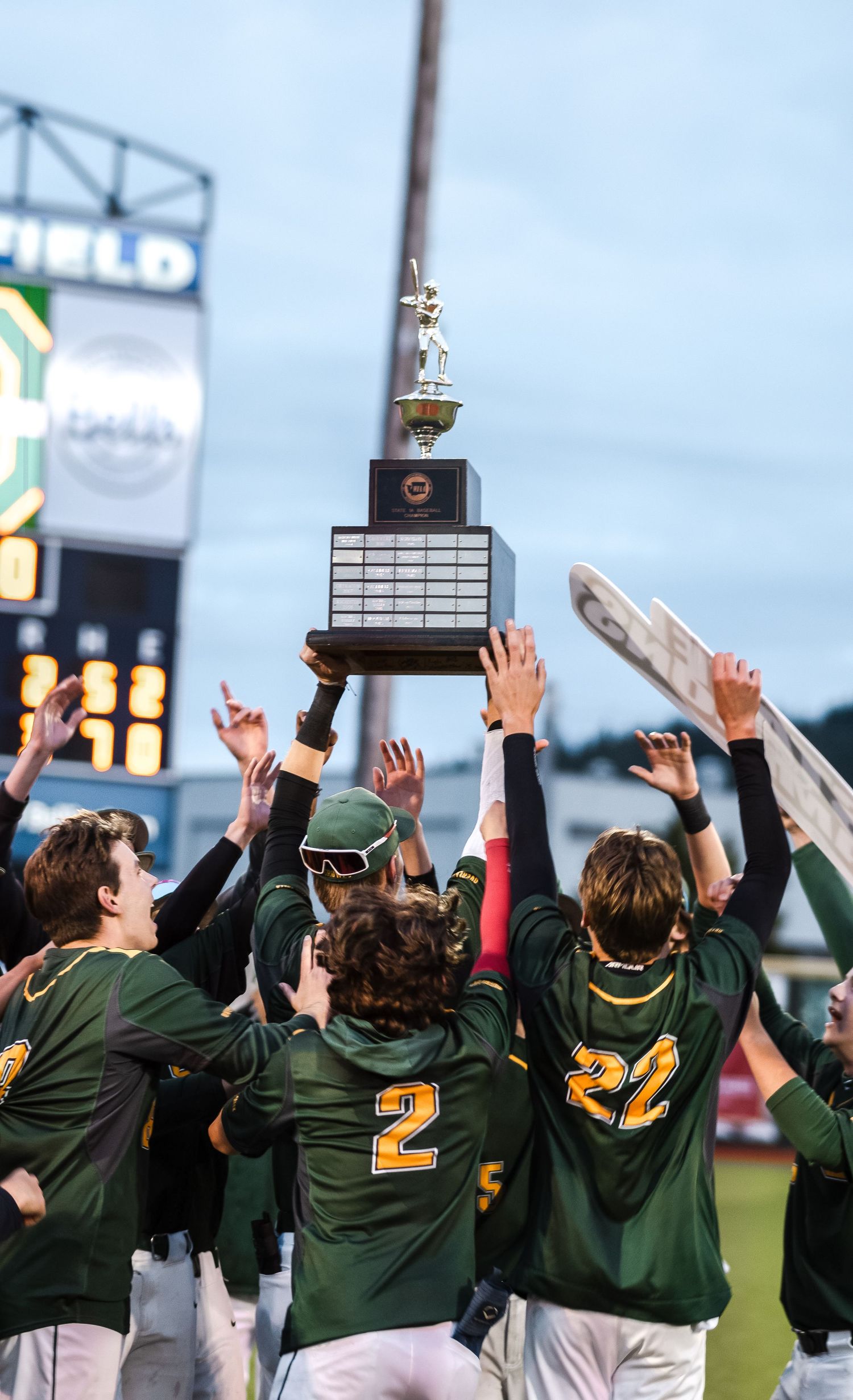 Baseball team in green uniforms celebrating victory with raised arms on a field.