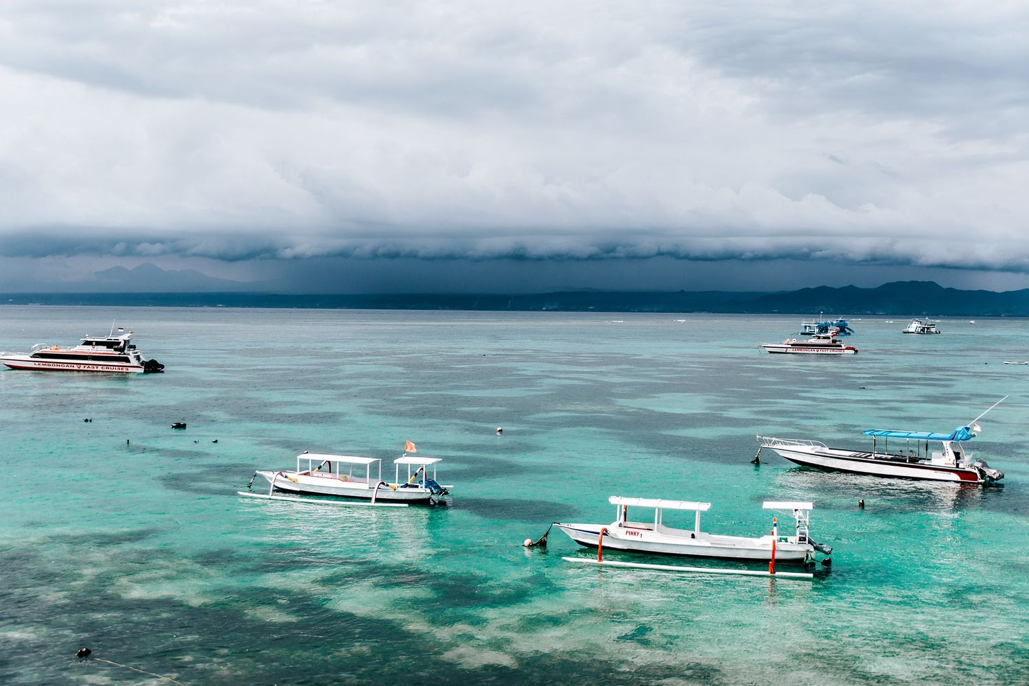 Boats floating on crystal clear turquoise waters near a tropical reef.