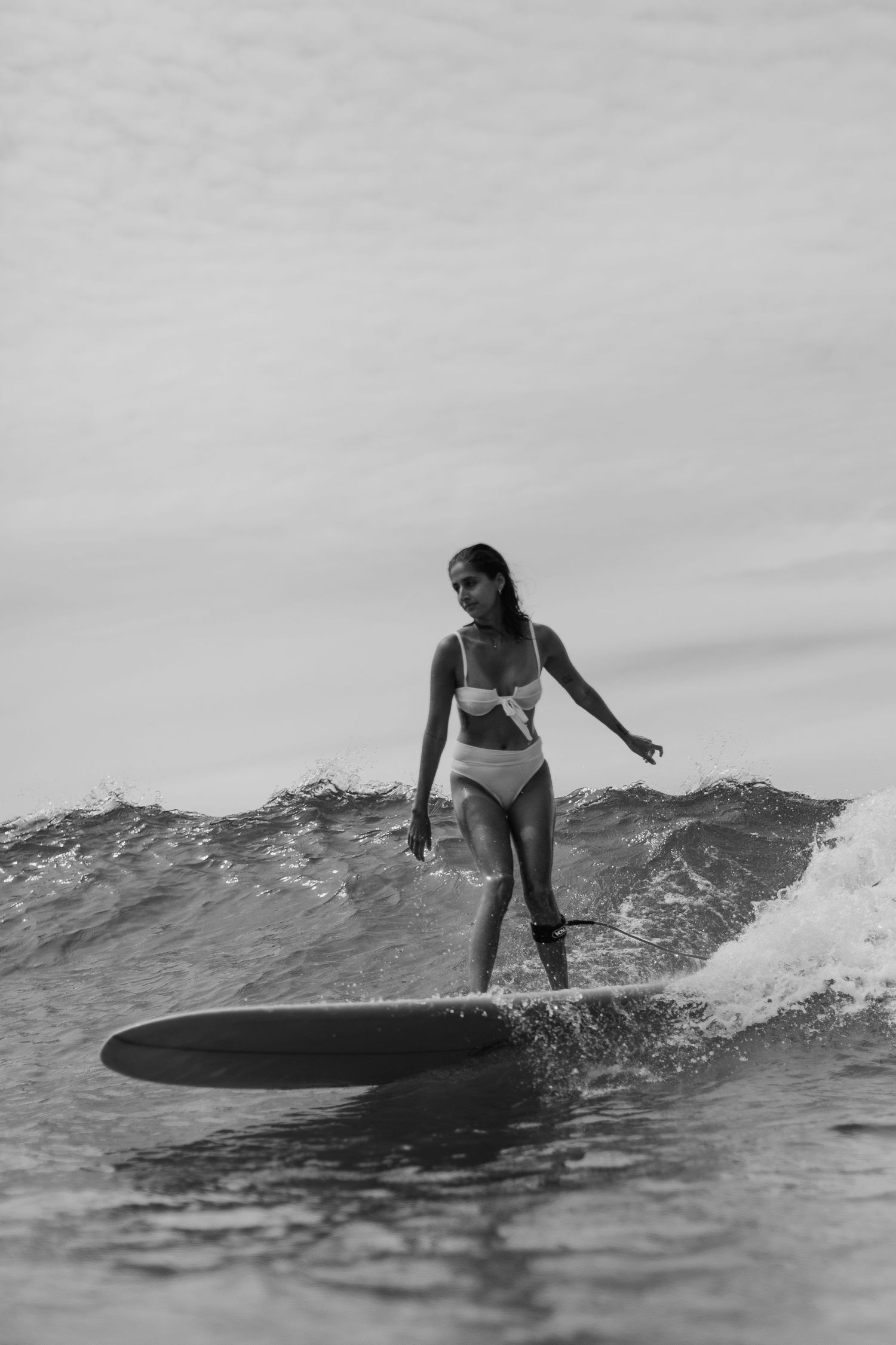 A surfer rides a rolling wave in black and white photography.