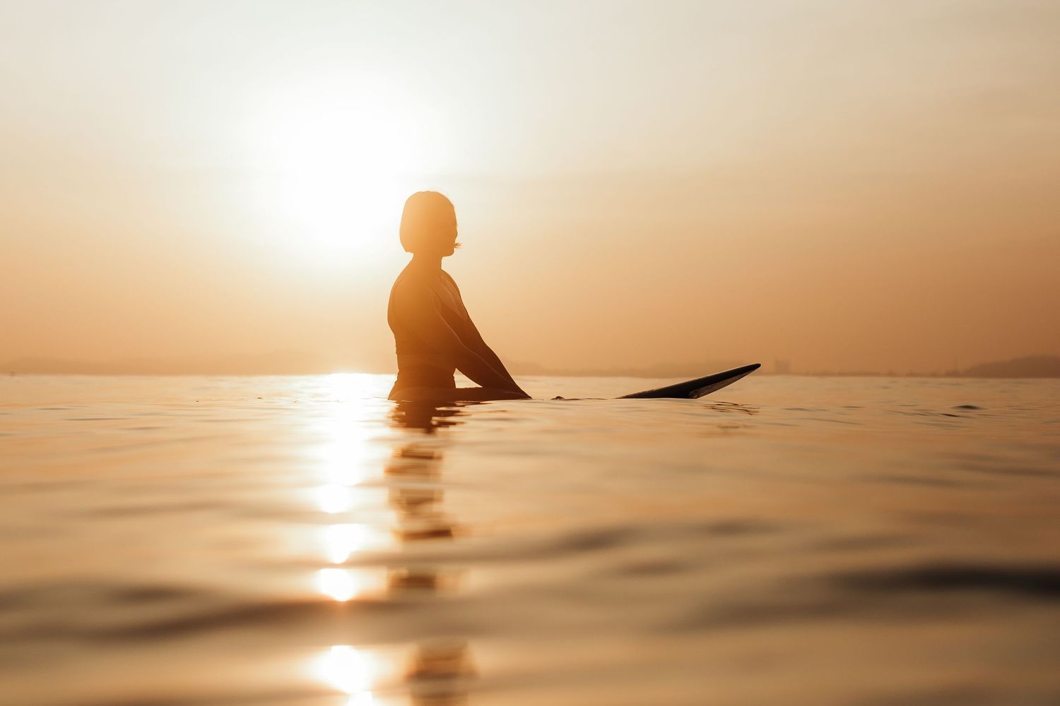 Silhouettes of swimmers in calm ocean waters during golden sunset.