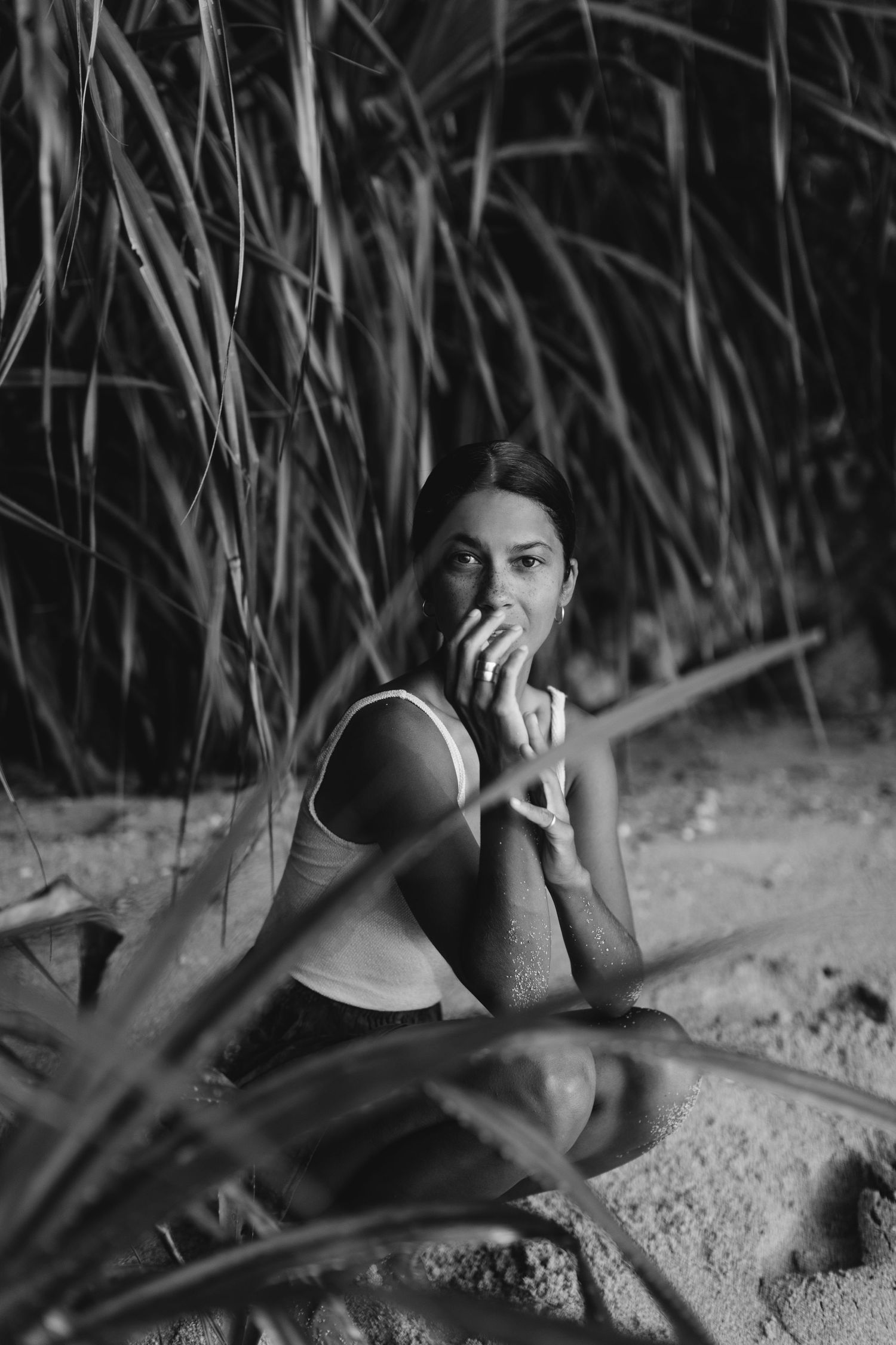 Person lying on sand beneath tropical foliage in black and white photography.