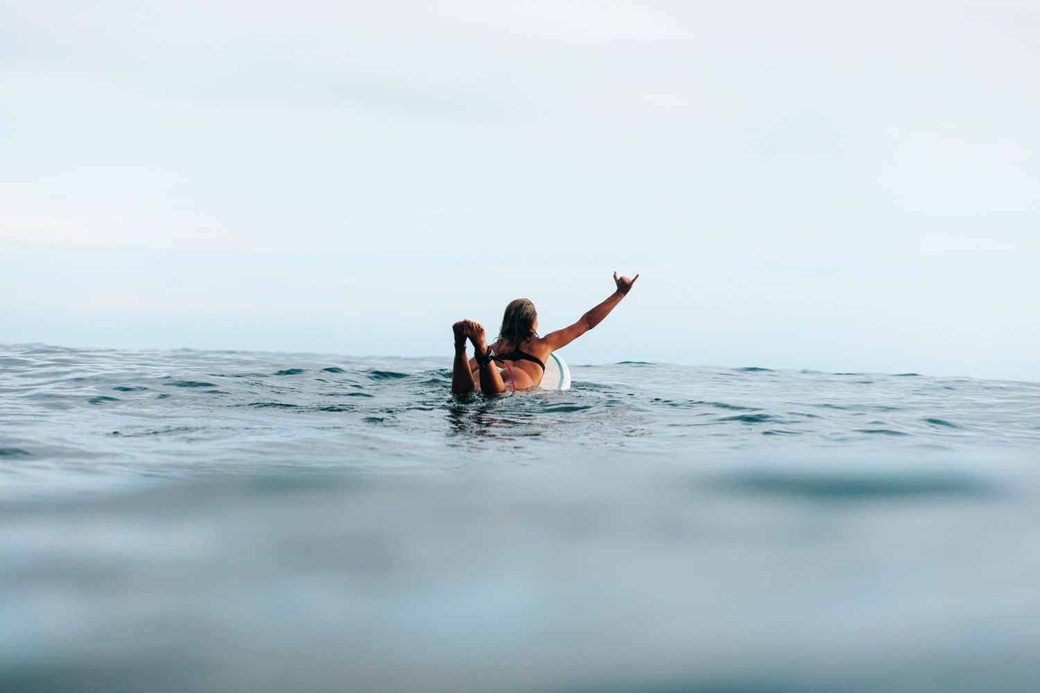 Surfer raising hand while swimming in ocean waves.