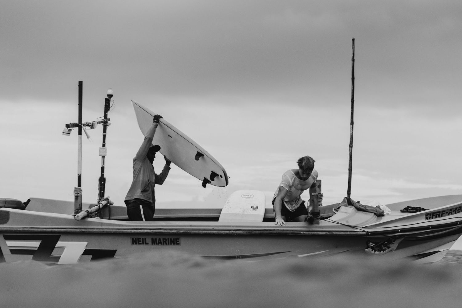 Two surfers preparing equipment on a boat in black and white.