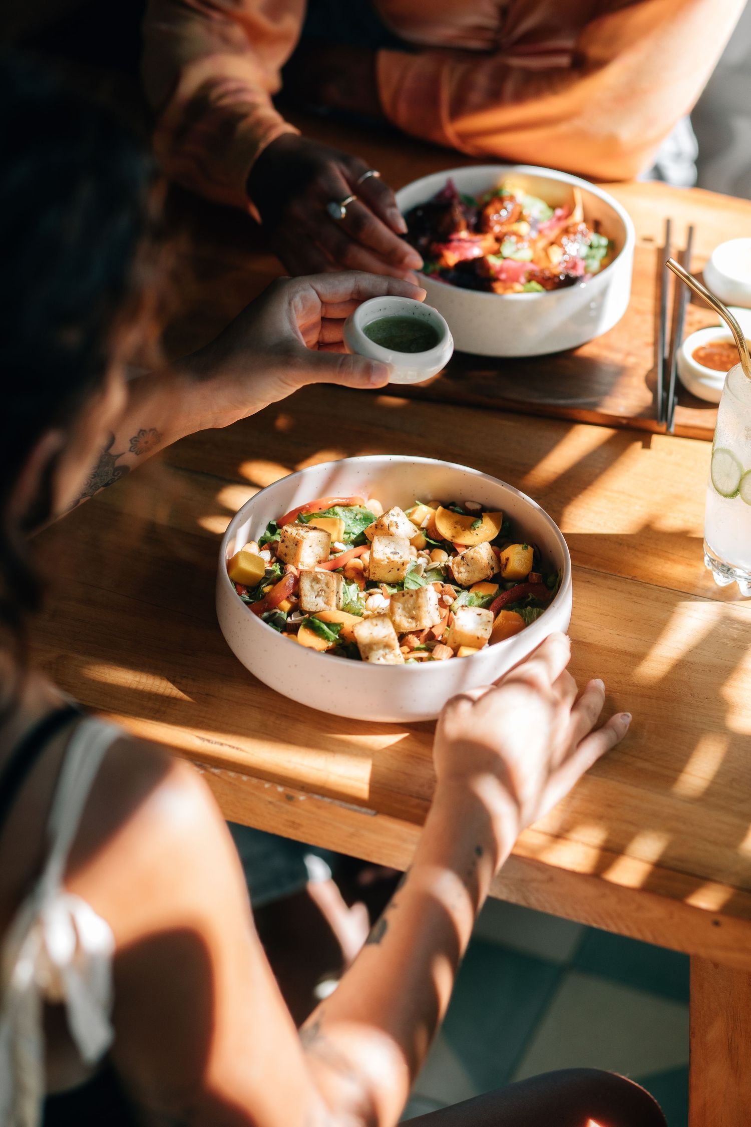 People sharing a meal at a wooden table with plates of food in warm sunlight.