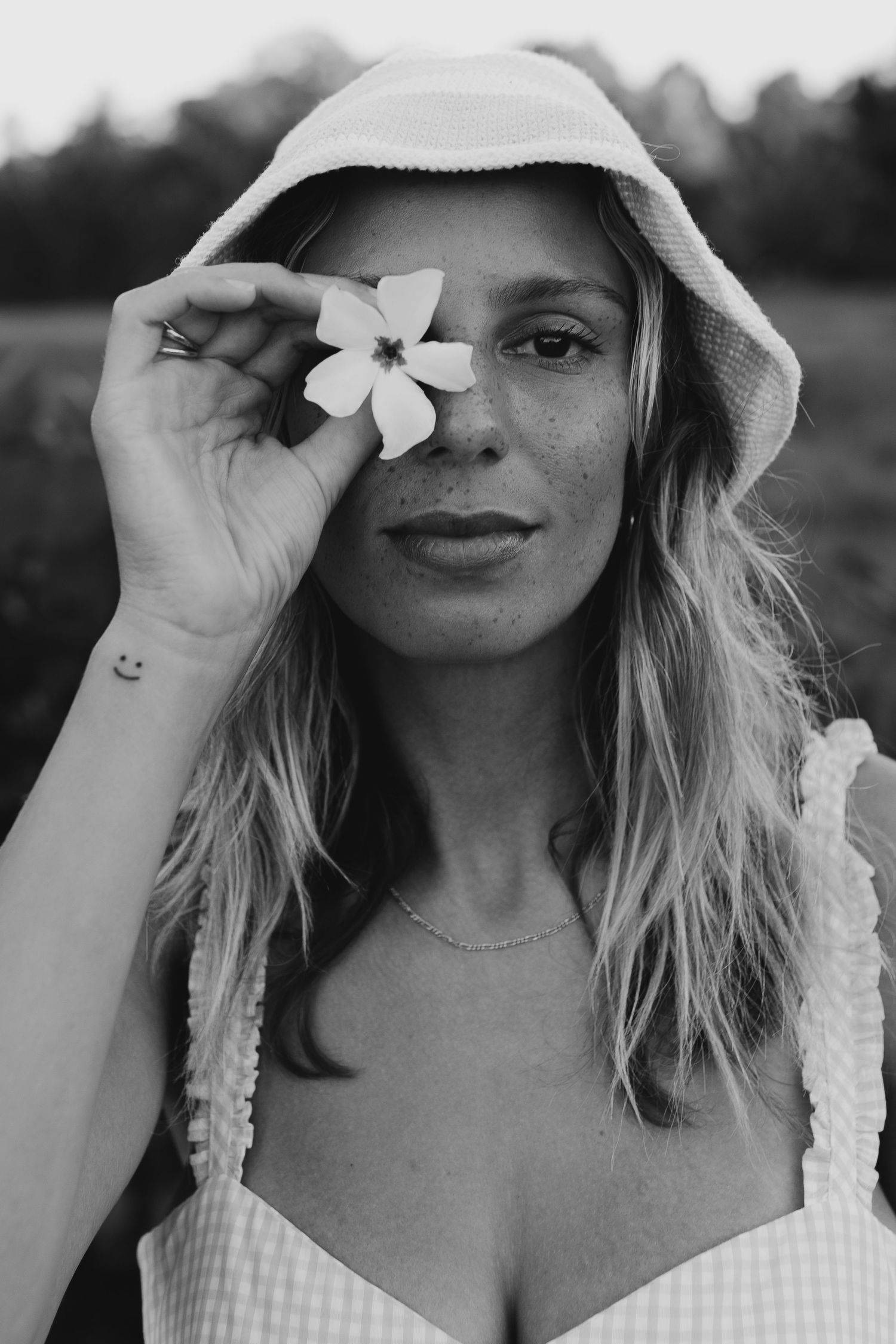 Woman in white sun hat holding flower petals in artistic black and white portrait.