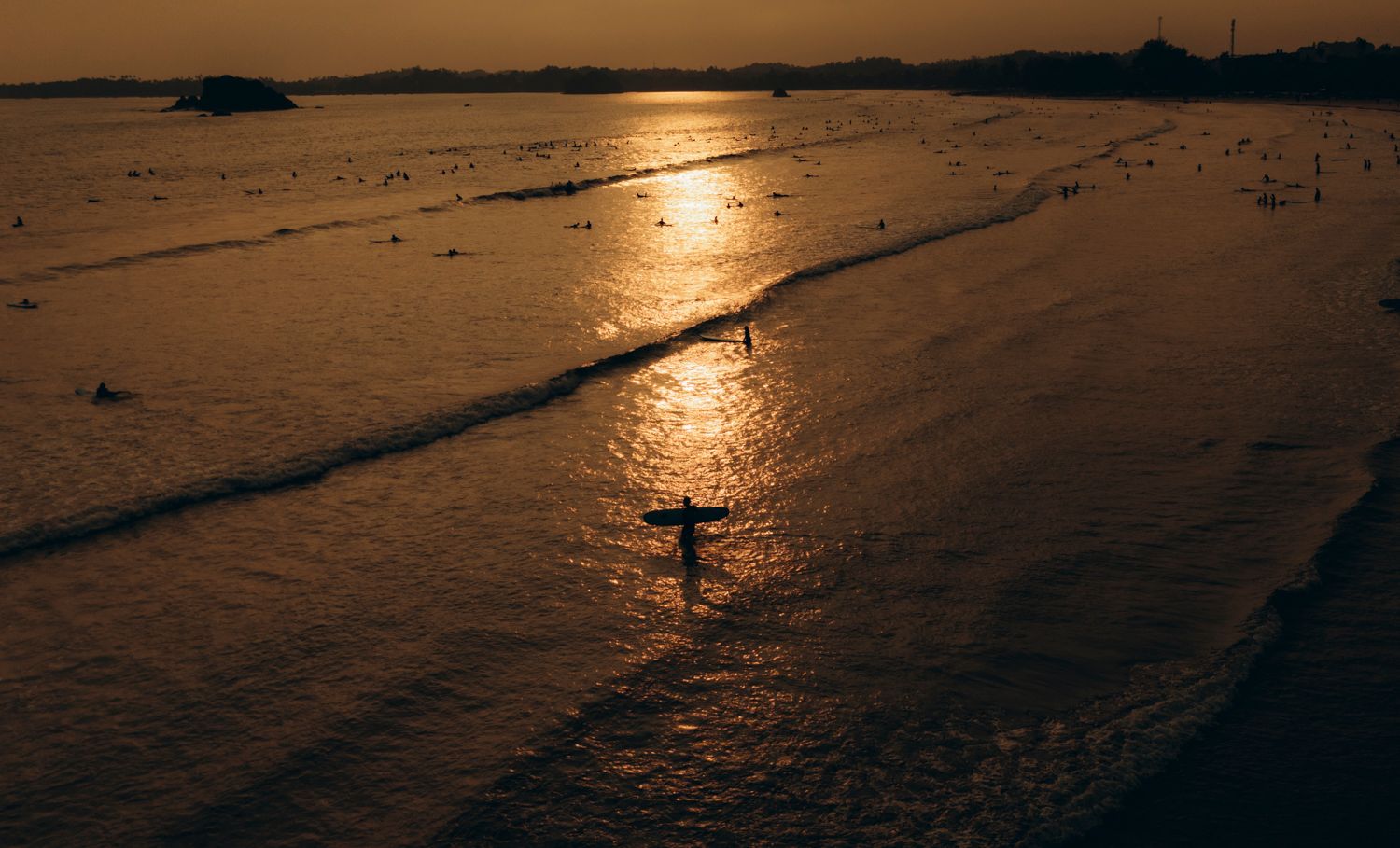 Silhouette of a surfer on a golden sunset beach with calm ocean waves reflecting warm light.