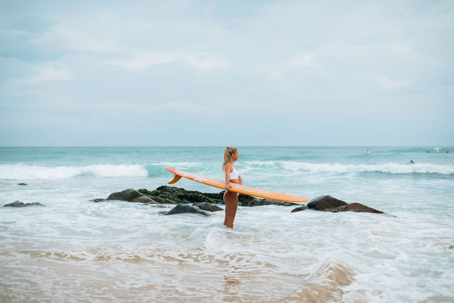 Surfer lounging on volcanic rocks as waves crash against tropical shoreline.
