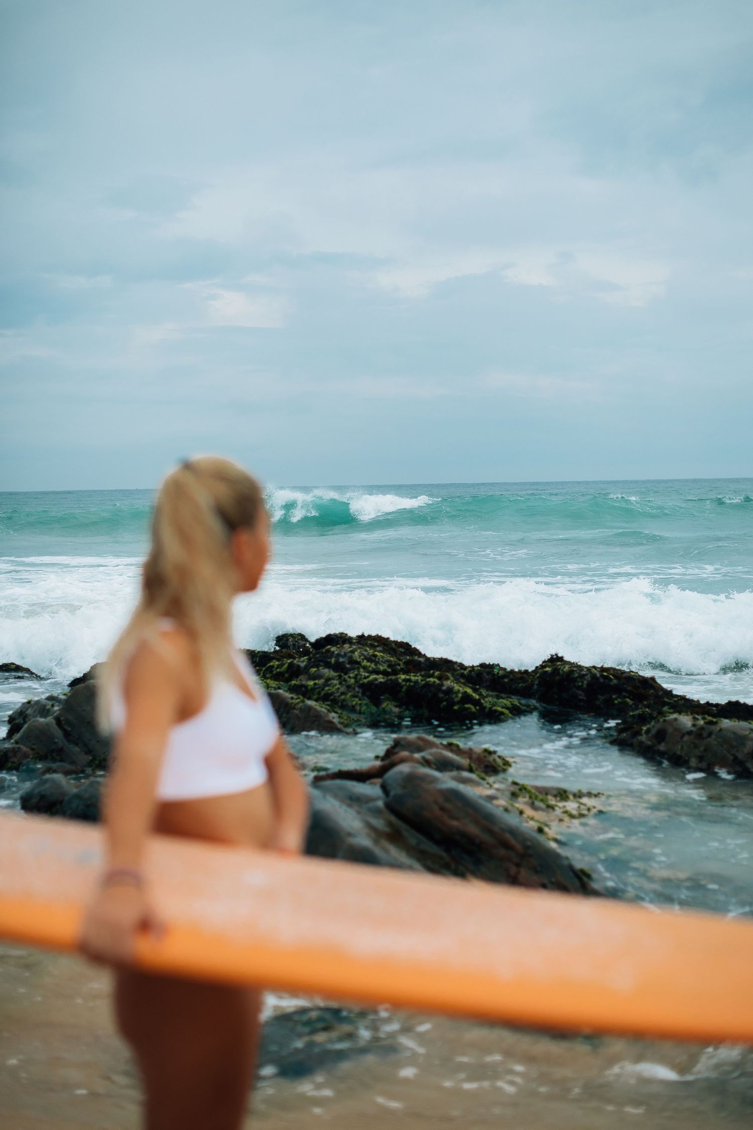 Blurred action shot of surfer carrying orange surfboard along rocky coastline.