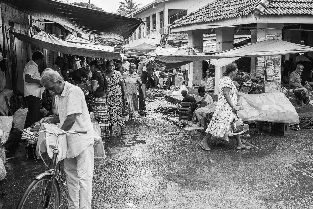 A bustling outdoor market scene with vendors and stalls under traditional roofing.