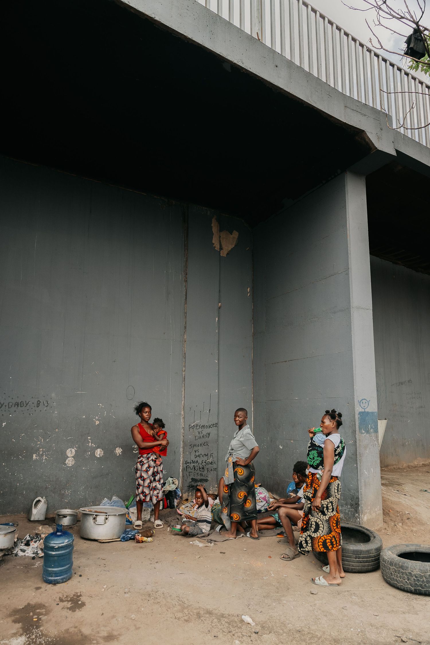 People gathered under a concrete overhang with scattered debris and tires.