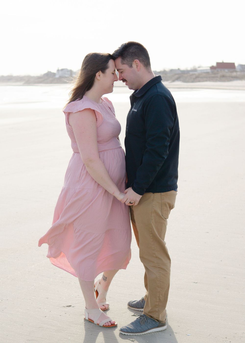 Tender seaside embrace, woman’s blush dress flowing around her during beach session.