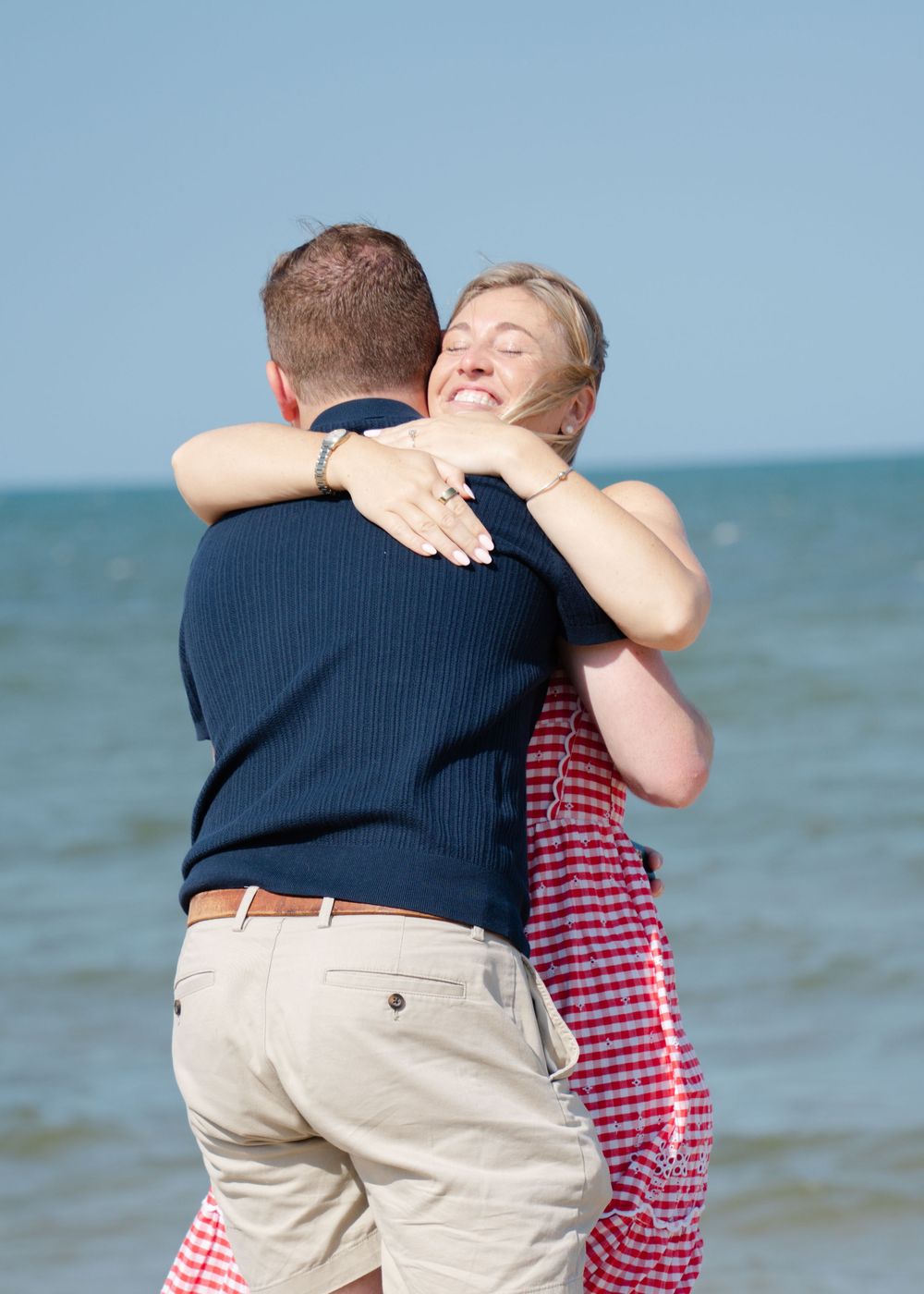 Just-engaged couple hugging emotionally on a Cape Cod beach, ocean waves in the background