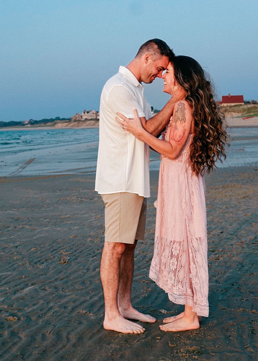 Candid beach photo, couple dressed in white and blush pink, embracing at golden hour