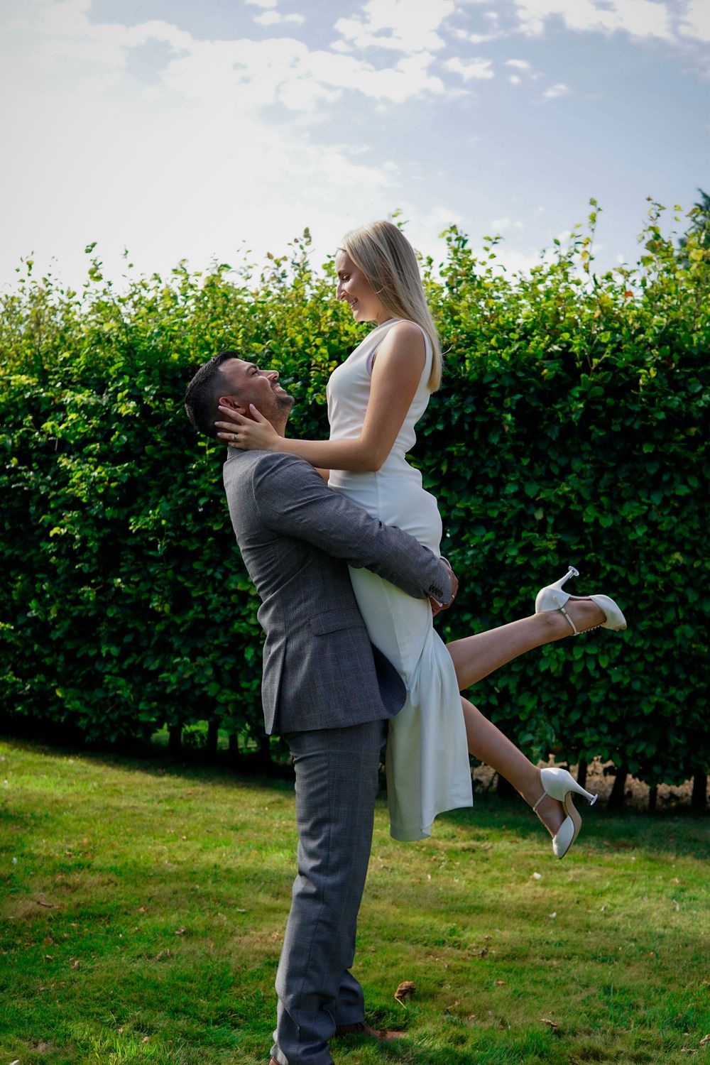 Romantic photo — couple sharing joyful lift and kiss among flowers and greenery.