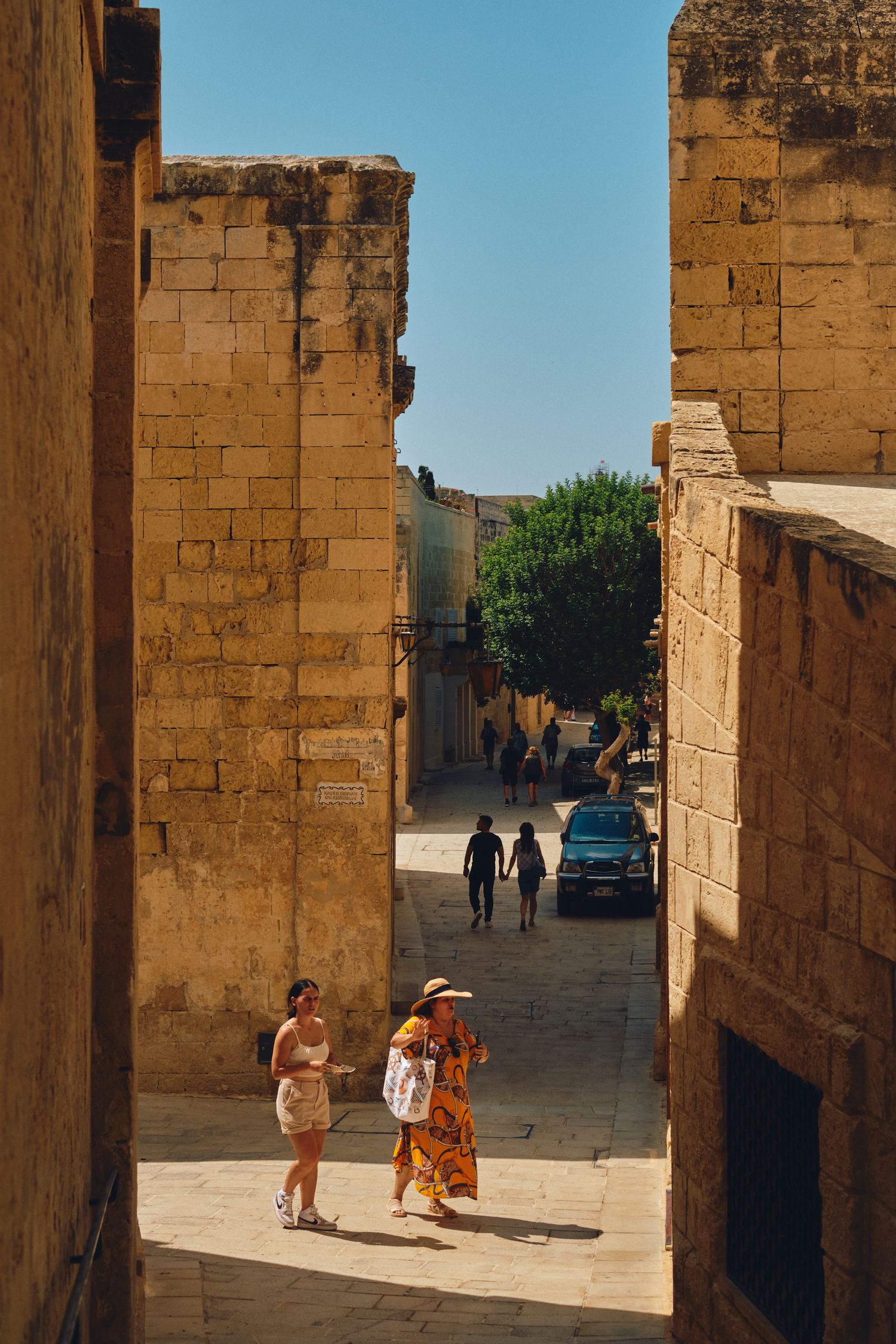People walking through narrow sandstone alleyway in Mediterranean town.