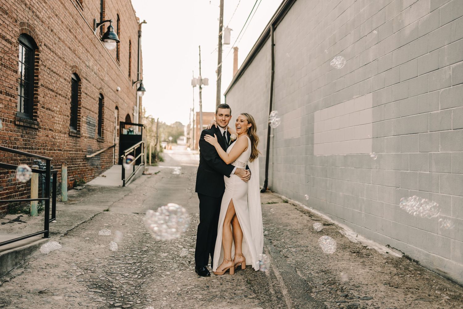 A couple in wedding attire shares an intimate moment in an urban alleyway.