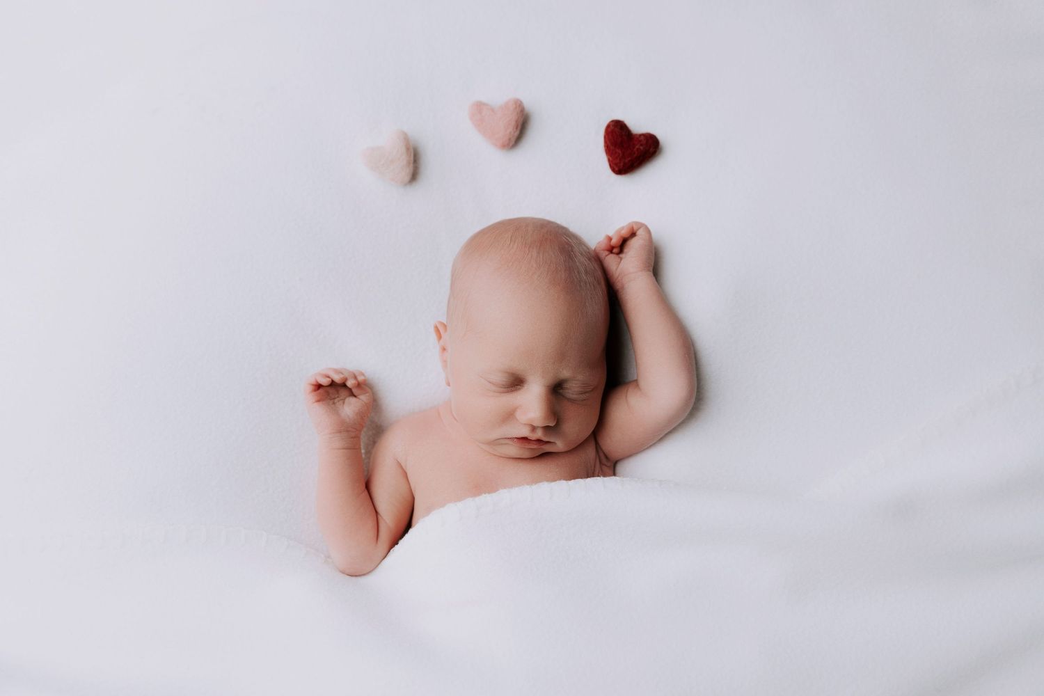 newborn baby girl on a white bed over a backdrop of three hearts