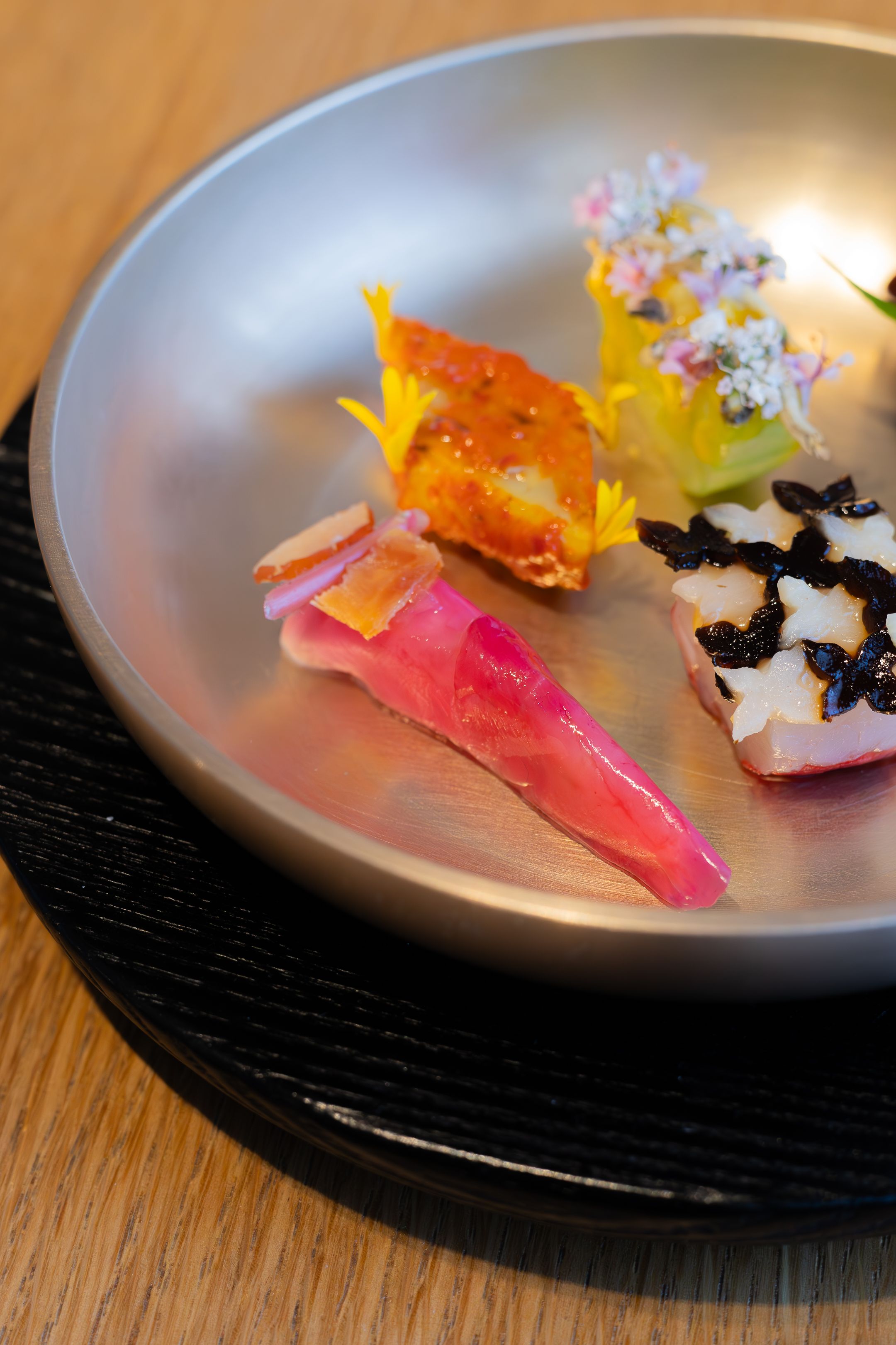 Elegant sushi plate featuring colorful garnishes and decorative elements on a metallic dish against a dark base.