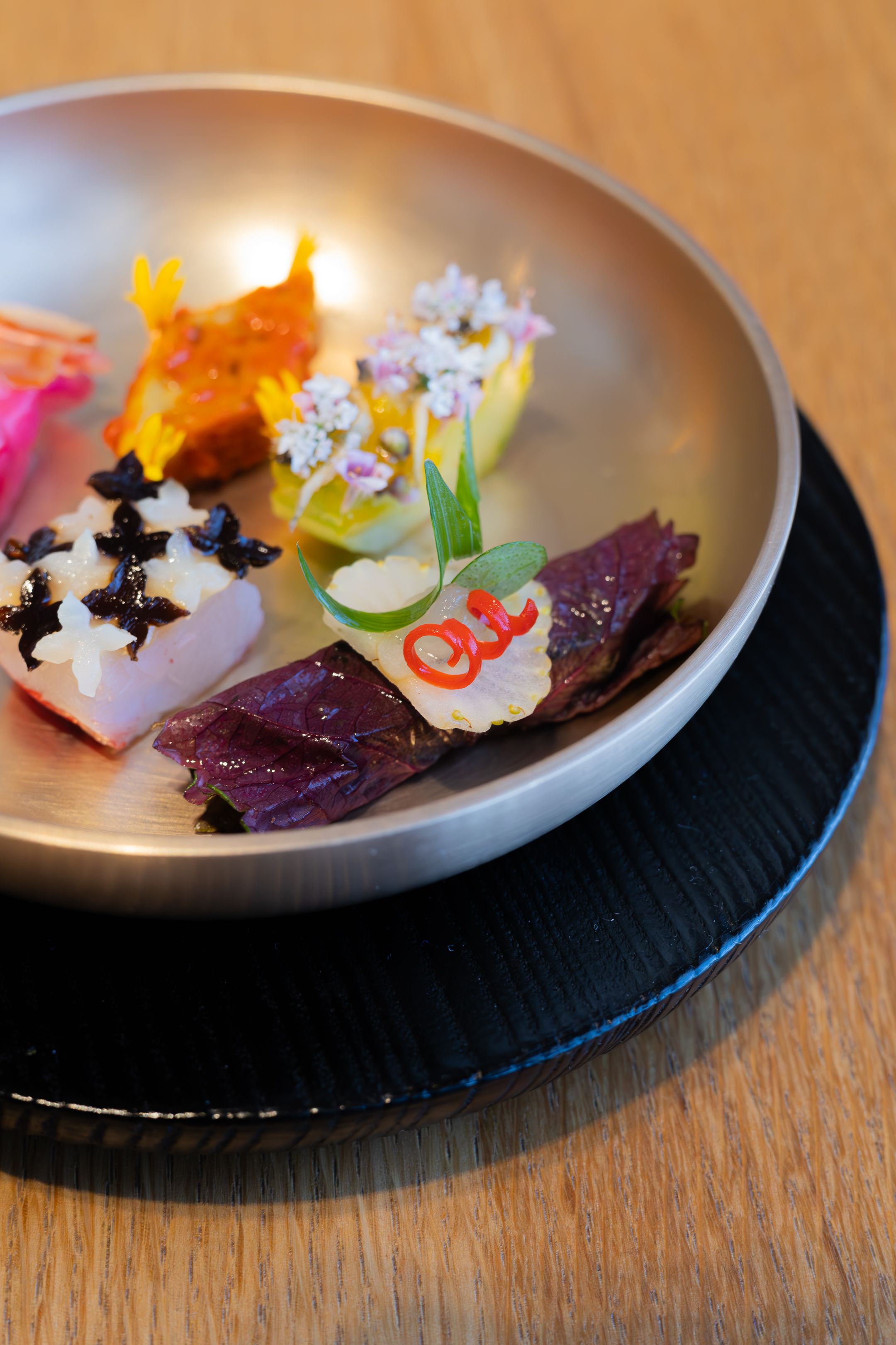 Modern sushi presentation with purple leaf, white fish, and citrus garnishes on a metallic plate.