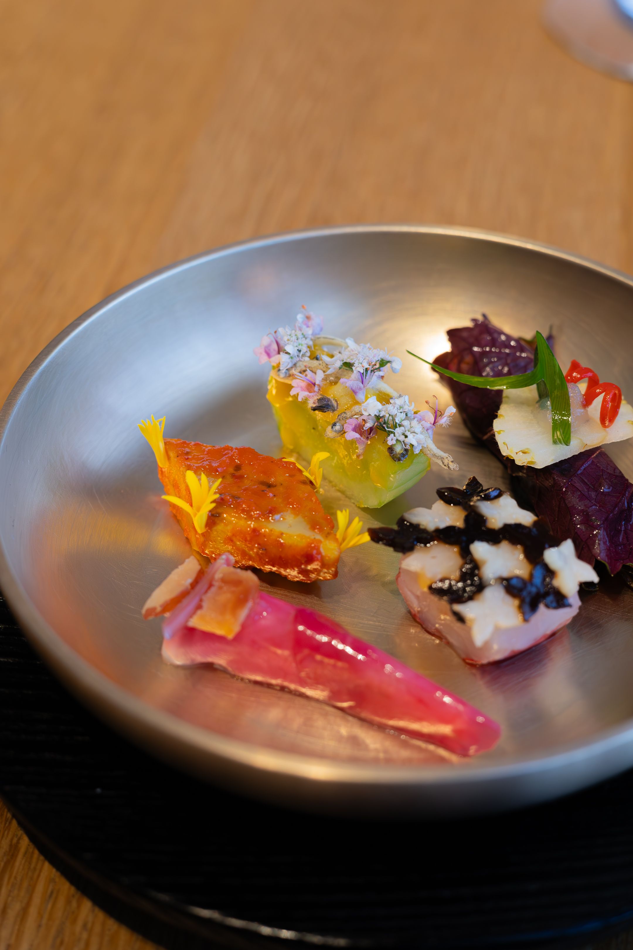 Artistic sushi arrangement with bright pink and orange elements on a curved silver plate.