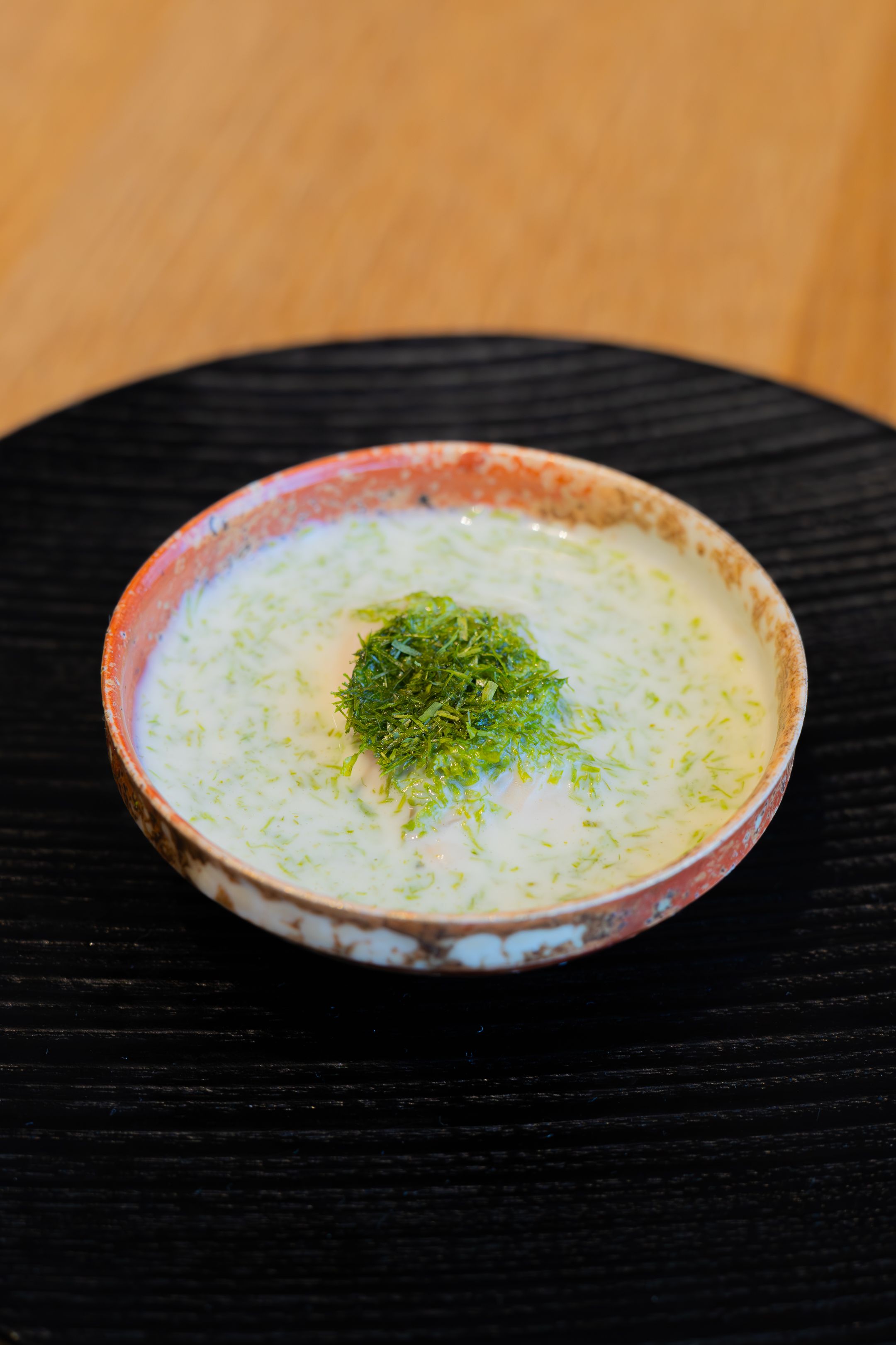 Close-up of a ceramic bowl containing pale soup with fresh green herbs on top.