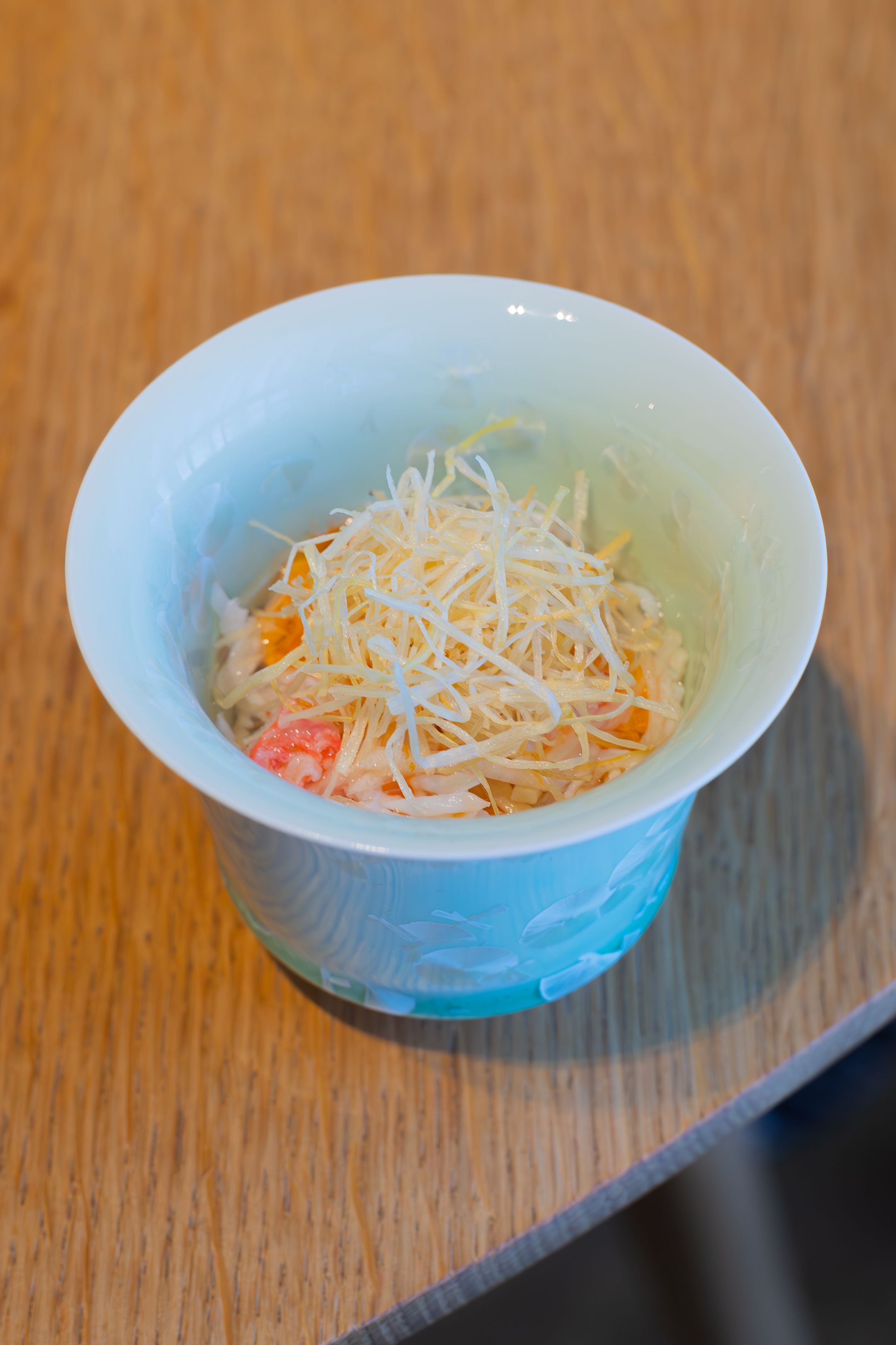 Blue-tinted bowl containing shredded vegetables and delicate garnishes.