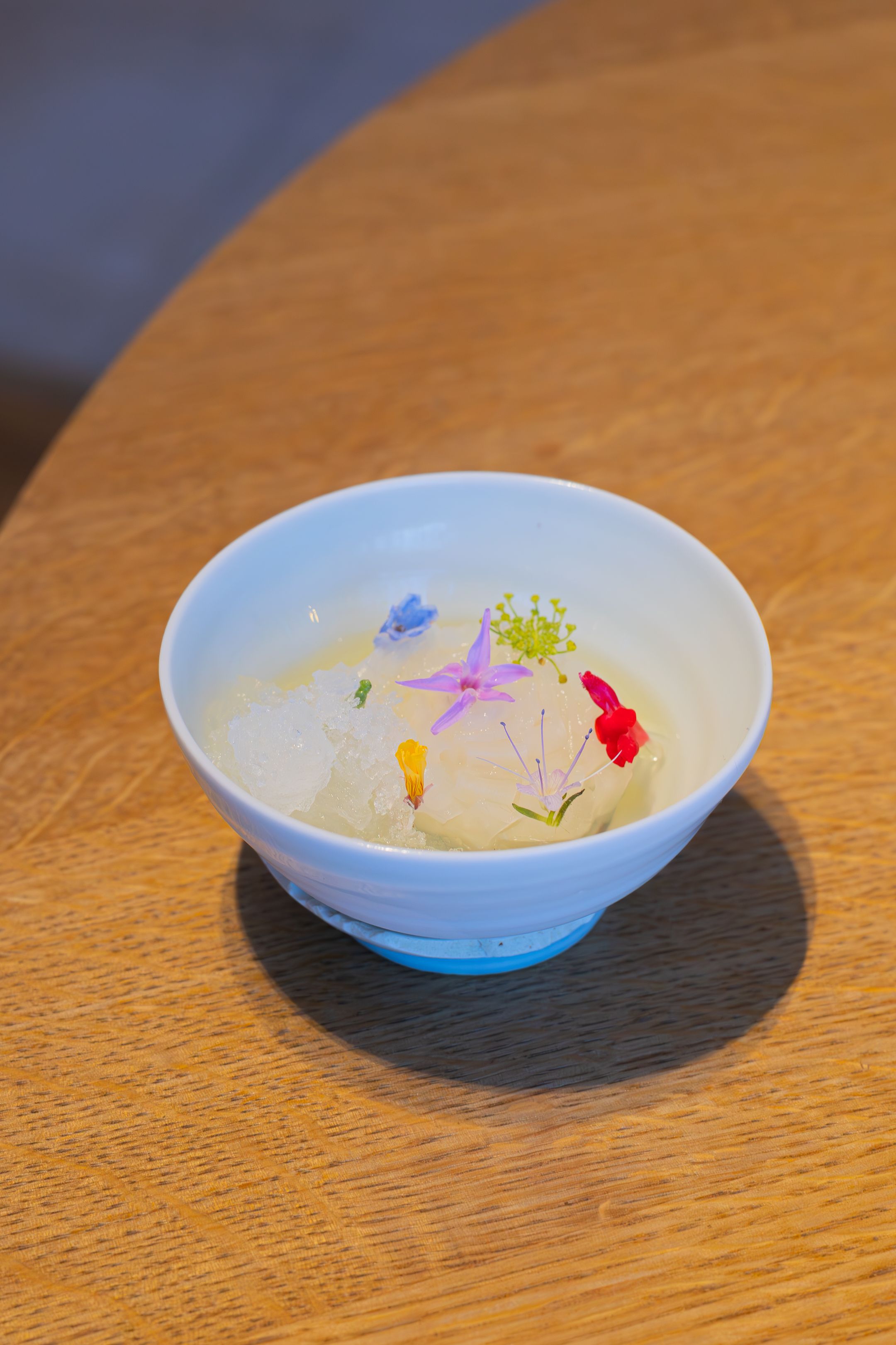 Clear broth soup decorated with colorful edible flower petals in a blue-gradient bowl.
