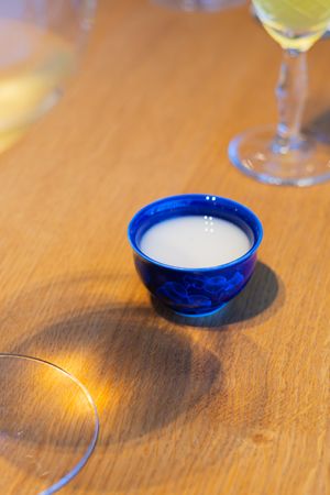 Blue ceramic sake cup filled with white liquid on wooden table.