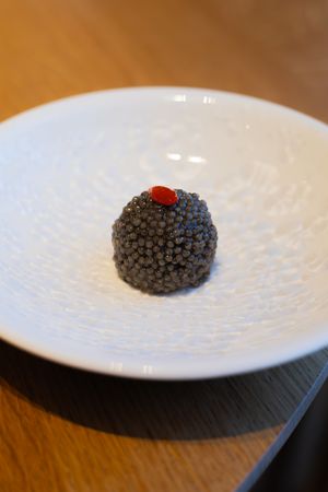 Spherical black caviar dish with red topping served on white plate.