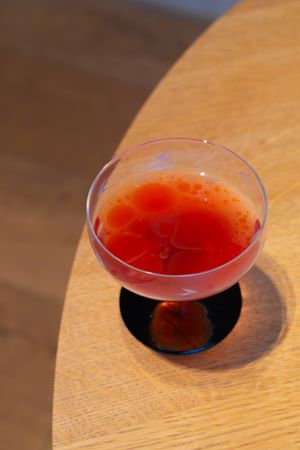 Red cocktail served in coupe glass on wooden table.