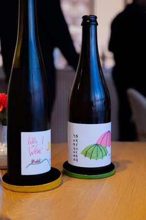 Two wine bottles with artistic labels featuring umbrella designs sitting on wooden coasters.