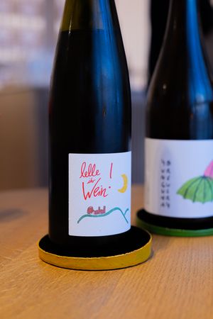 Close-up of wine bottle with whimsical hand-drawn label design on wooden surface.