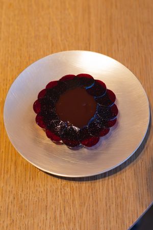 Circular chocolate dessert with berry garnish served on white plate.