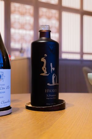 Black bottle of Hwayo spirits with minimalist design on wooden table.