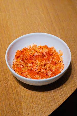 Orange-red spicy seasoning or caviar served in a small white ceramic bowl.