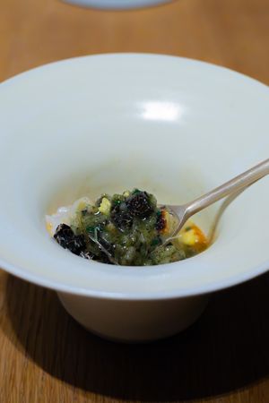 Close-up of a white bowl containing broccoli and dark ingredients with a spoon.