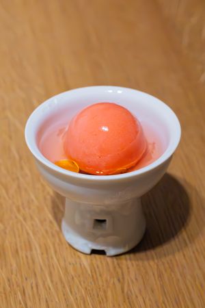 Bright orange sorbet served in a white ceramic pedestal bowl against wooden surface.